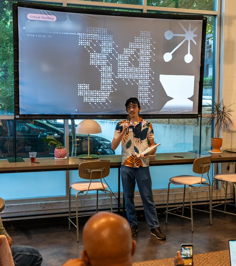 An attendee pitching with a microphone in front of the pitch display, which shows the Critical Thinking problem, the pitch idea and a large countdown.