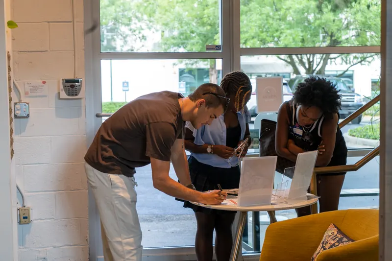 Three attendees bent over the pitch sign-up sheets at a small table by the entrance.