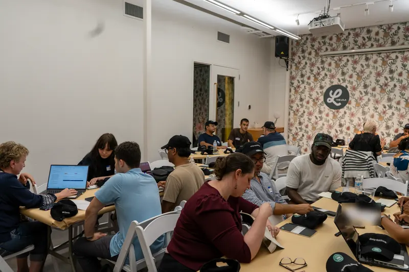 Teams at long tables in a side room with laptops and notebooks, starting to work.