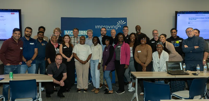 Workshop attendees gathered for a group photo in a corporate training room, with Claude session slides on the screens behind them